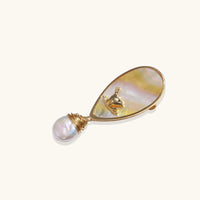 Angled view of iridescent shell bird brooch with gold frame and wire-wrapped baroque pearl | Olaty