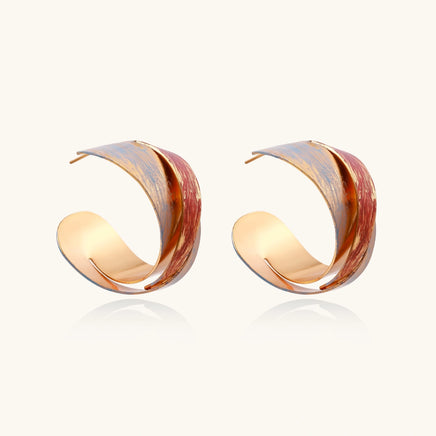 Sculptural gold-plated hoop earrings with diagonal purple and coral enamel stripes in twisted ribbon design