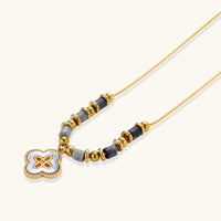 Close-up of gold-tone necklace with grey stone beads and iridescent quatrefoil pendant | Olaty
