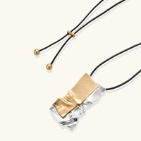 Two-tone sculptural pendant necklace on black adjustable cord with gold-tone end details | Olaty