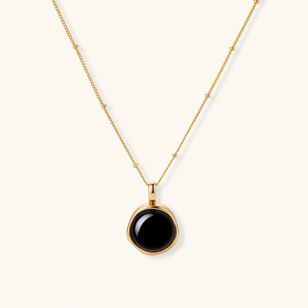Circular black agate pendant on gold-plated sterling silver chain against cream background, showing modern minimalist design.