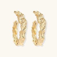 Angled pair of sculptural gold-tone hoops with raised molten surface texture and irregular edges | Olaty