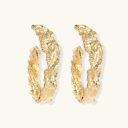 Angled pair of sculptural gold-tone hoops with raised molten surface texture and irregular edges | Olaty
