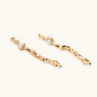 Angled view of gold-tone molten flow earrings with white pearl centers and long organic silhouettes | Olaty