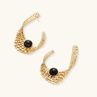 Angled view of gold sculptural mesh earrings with black resin cabochon accents and woven openwork texture | Olaty