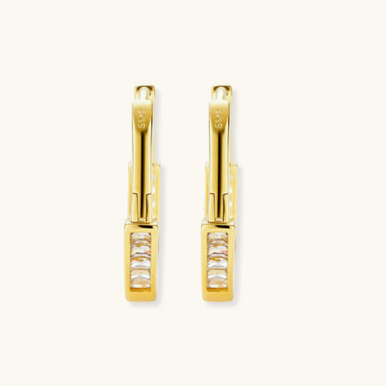 Close-up of gold-plated sterling silver huggie hoop earrings featuring rectangular cubic zirconia stones on neutral background.