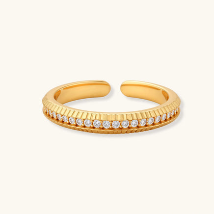 Adjustable gold-plated ring with row of sparkling crystals on ribbed band, shot against cream background