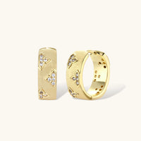 Gold-plated hoop earrings with textured surface and raised floral motifs set with clear zirconia stones on cream background.