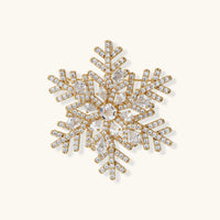 Ornate gold-plated snowflake brooch with geometric crystal pattern and sparkling zirconia stones on cream background.