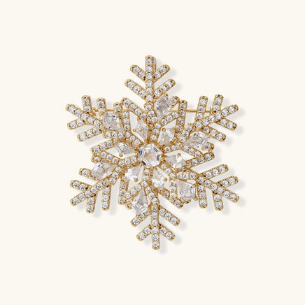 Ornate gold-plated snowflake brooch with geometric crystal pattern and sparkling zirconia stones on cream background.