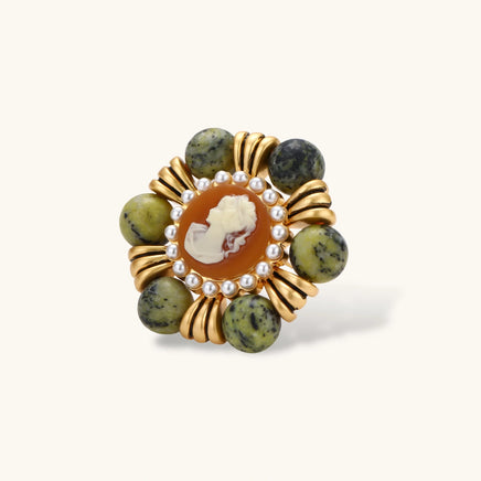 Ornate gold-plated brooch with central cameo, radiating spokes, pearl border, and green marbled natural stones on white background.