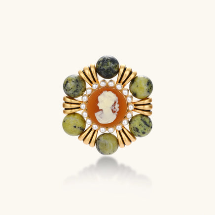 Ornate gold-plated brooch with central cameo, radiating spokes, pearl border, and green marbled natural stones on white background.