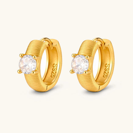 Angled pair of brushed solitaire huggie hoop earrings with round cubic zirconia stones and hinged closures | Olaty