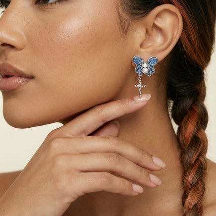 Close-up of royal blue denim butterfly earring with pearl center, sculptural silver-tone wings and cross drop charm | Olaty