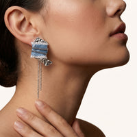 Close-up of blue denim statement earring with silver-tone chain accents, sculptural metal details and dangling chains | Olaty