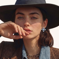 Model wearing blue denim flower statement stud earrings with pearl centers and sparkling zirconia accents | Olaty