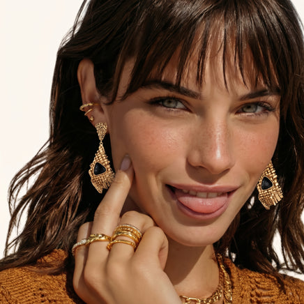 Close-up styling of long gold-tone mesh drop earrings with glossy black resin centers | Olaty