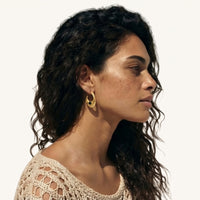 Side view of sculptural gold woven earrings with glossy black resin accents worn on the ear | Olaty