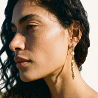 Close-up side view of gold-tone organic flow earring with round white pearl accent worn on model | Olaty