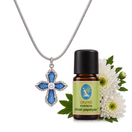 Silver cross diffuser necklace with blue denim detailing displayed beside an amber essential oil bottle with white flowers | Olaty