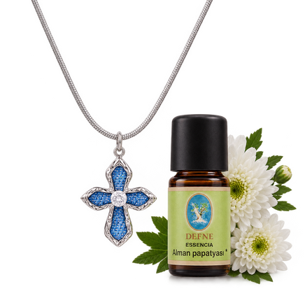 Silver cross diffuser necklace with blue denim detailing displayed beside an amber essential oil bottle with white flowers | Olaty