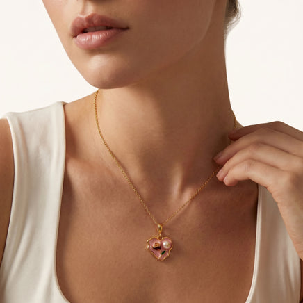 Close-up of model wearing pink heart pendant necklace with floral enamel and pearl detail | Olaty