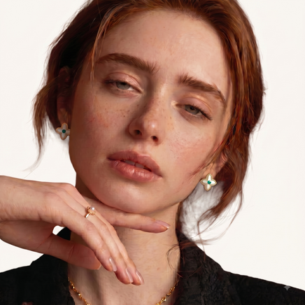 Model wearing gold-tone Mother of Pearl clover stud earrings with green gemstone centers | Olaty