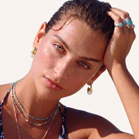 Model wearing sculptural cone hoop earrings with polished gold finish and white resin drops | Olaty