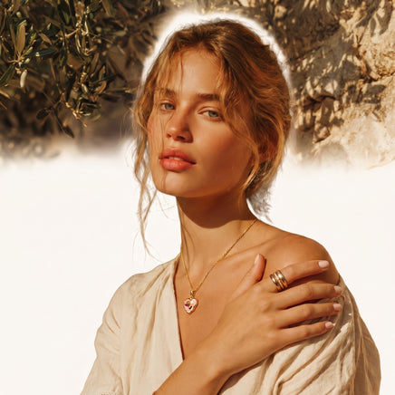 Model wearing pink heart pendant necklace with gold chain in warm outdoor setting | Olaty