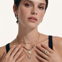 Model layering gold-tone necklaces including grey stone bead necklace with iridescent clover pendant | Olaty