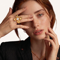 Close-up of model wearing sculptural four-petal gold-tone flower ring with white pearl center | Olaty