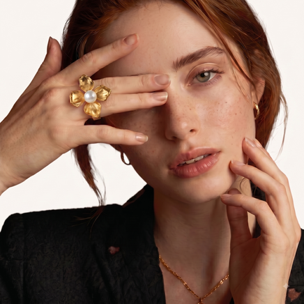 Close-up of model wearing sculptural four-petal gold-tone flower ring with white pearl center | Olaty