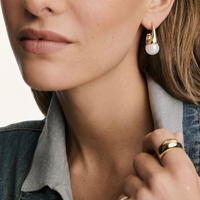 Close-up of model wearing sculptural cone hoop earring with polished gold finish and white resin drop | Olaty