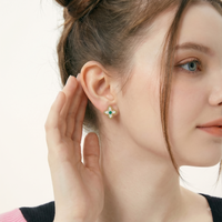 Close-up of model wearing gold-tone clover stud earring with Mother of Pearl petals and green gemstone center | Olaty